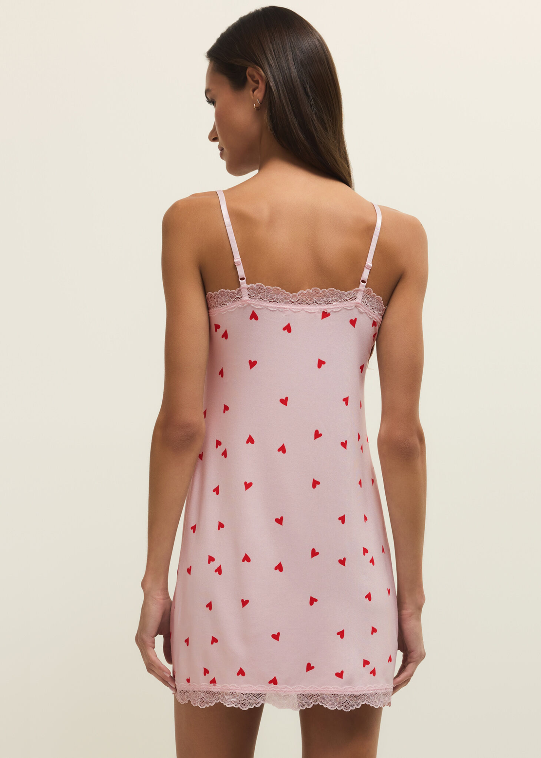 Woman turned around wearing a pink nightgown with red hearts and pink lace trim