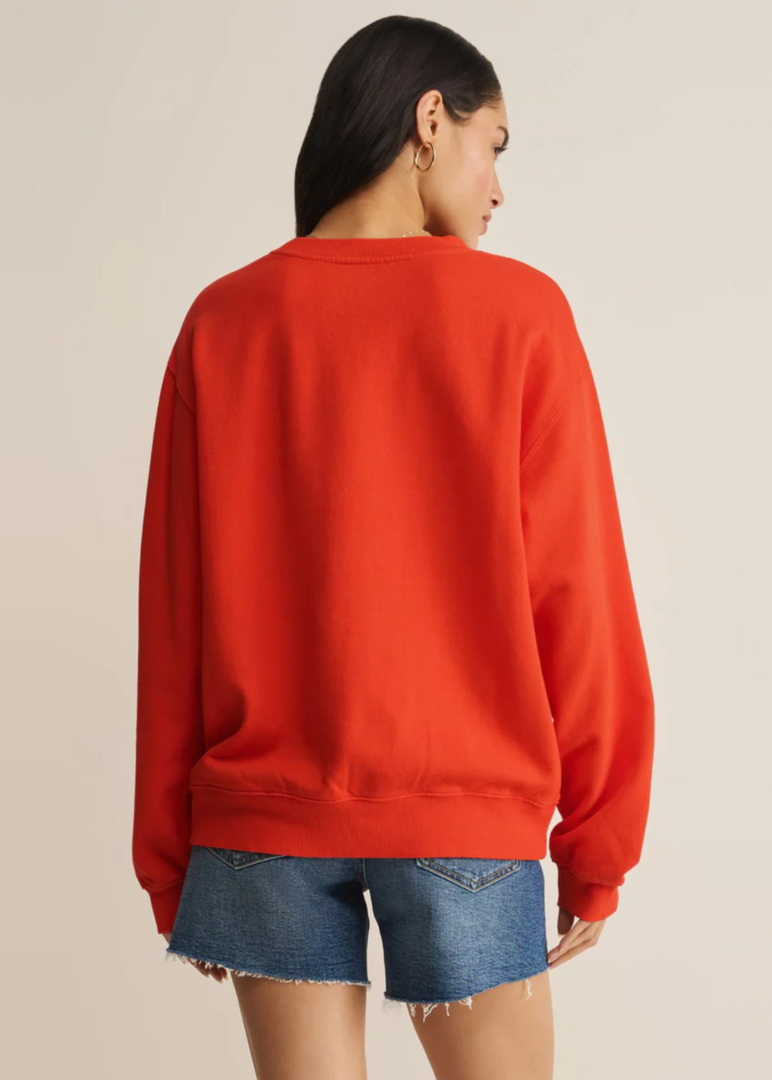 Woman turned around wearing a red sweatshirt with denim shorts