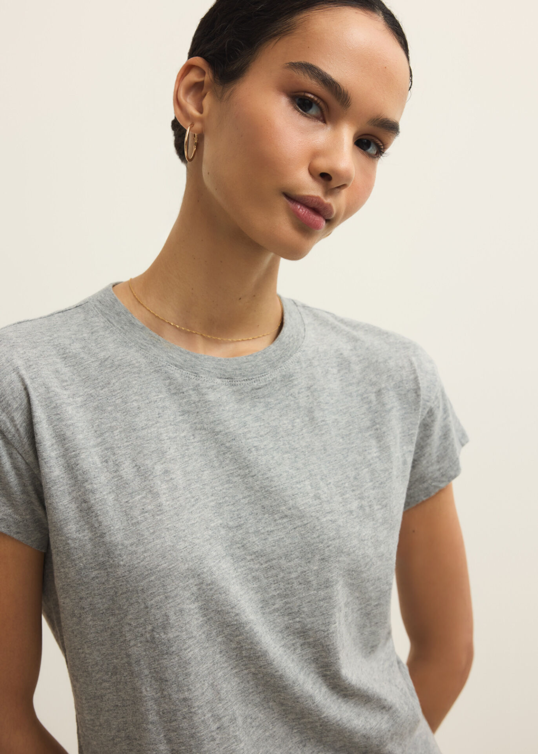 Close up of a woman wearing a grey short sleeve t-shirt and jeans against a grey background