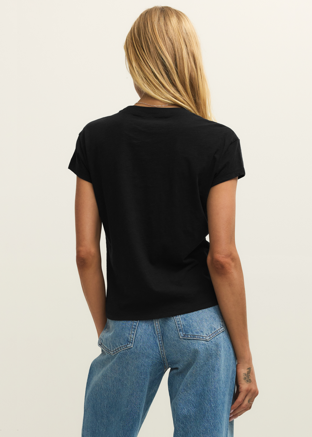 Woman turned around wearing a black tee shirt with jeans in front of a white background