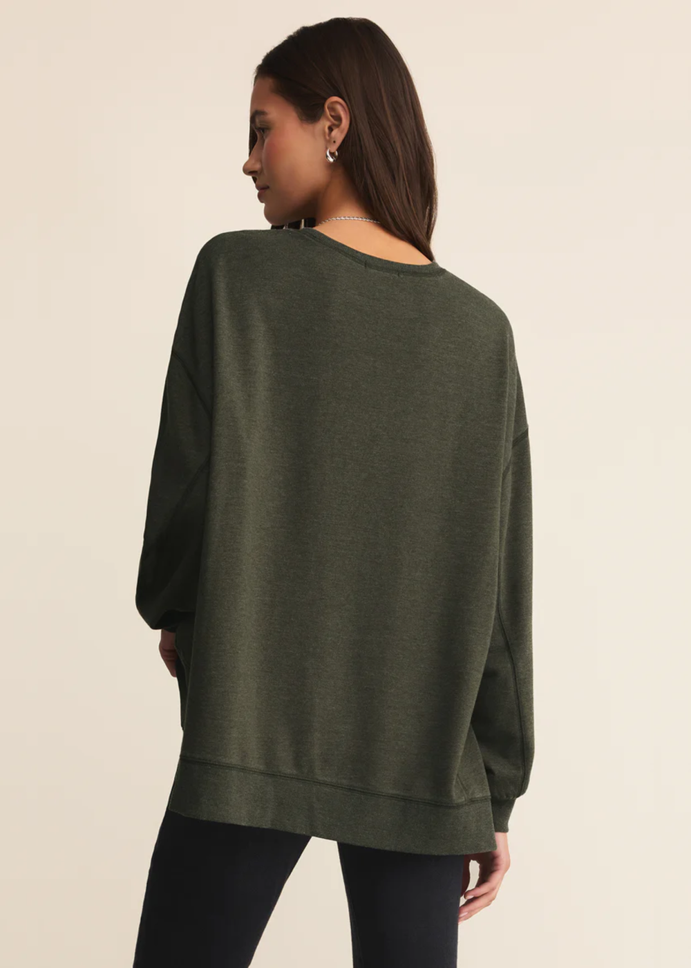 Woman turned around wearing a dark green sweatshirt with black pants standing in front of a white background