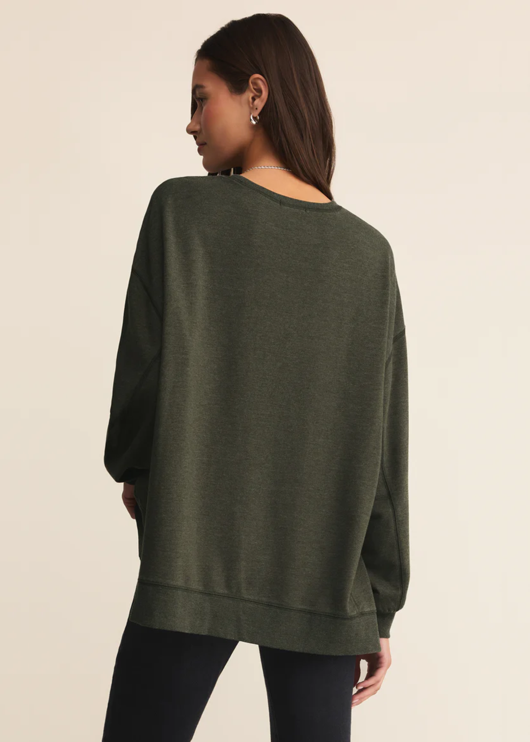 Woman turned around wearing a dark green sweatshirt with black pants standing in front of a white background