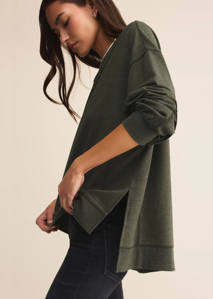 Woman turned to the side wearing a dark green sweatshirt with black pants standing in front of a white background