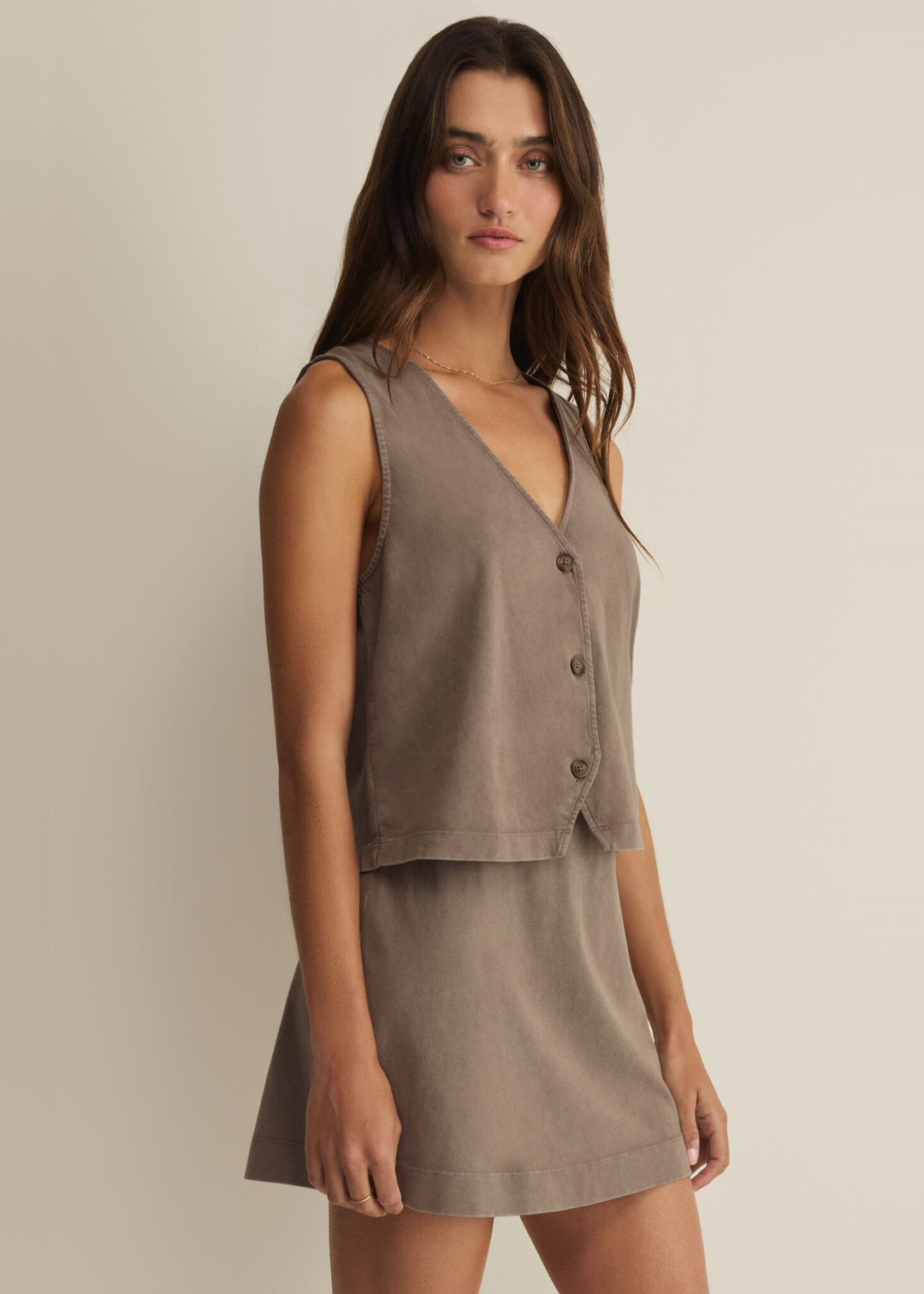 Woman wearing a taupe button up tank top with a matching skirt