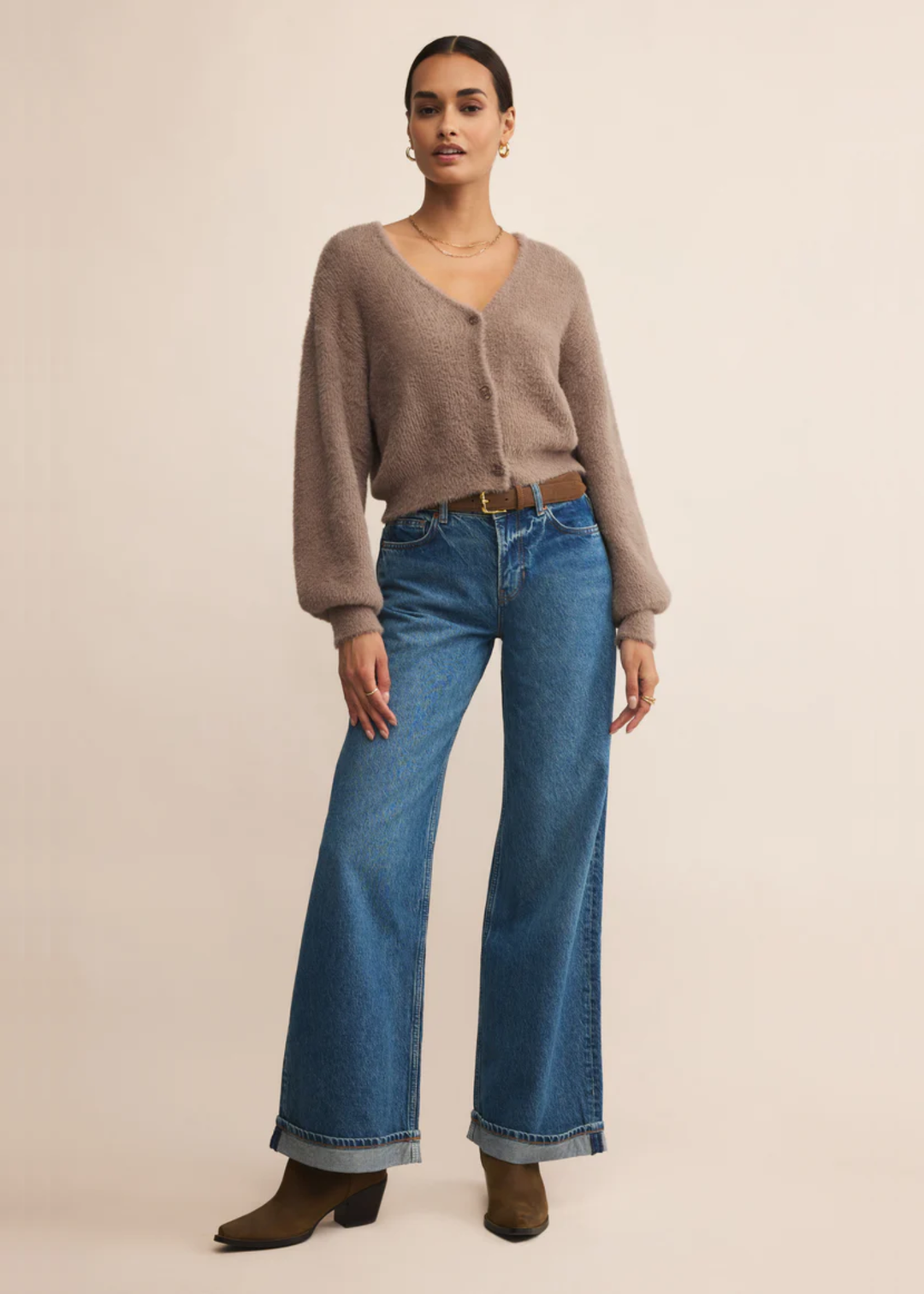 Woman wearing a fuzzy light brown cardigan with jeans in front of a grey background