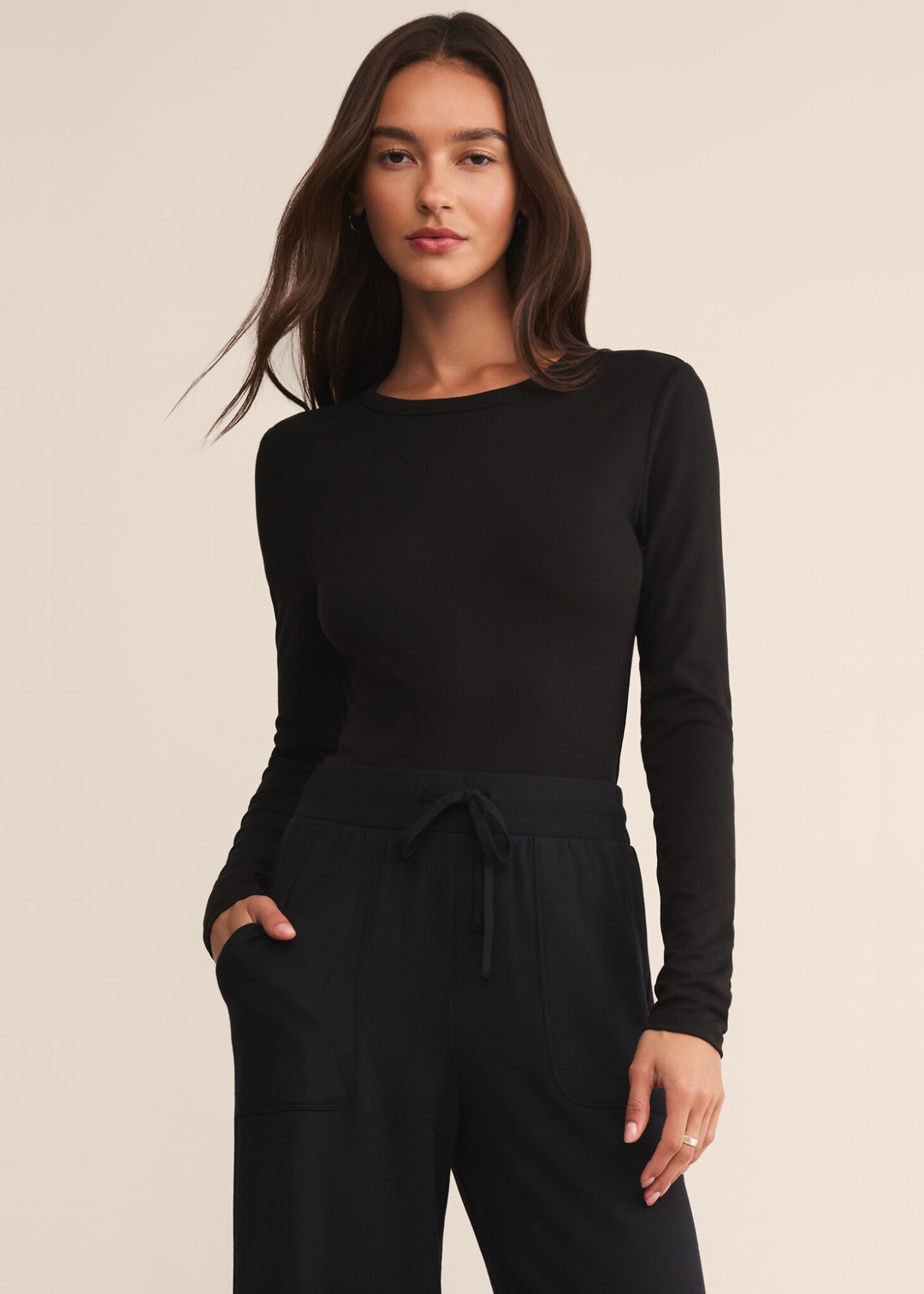 Woman wearing a long sleeve black crew neck shirt with black pants and standing in front of a white background