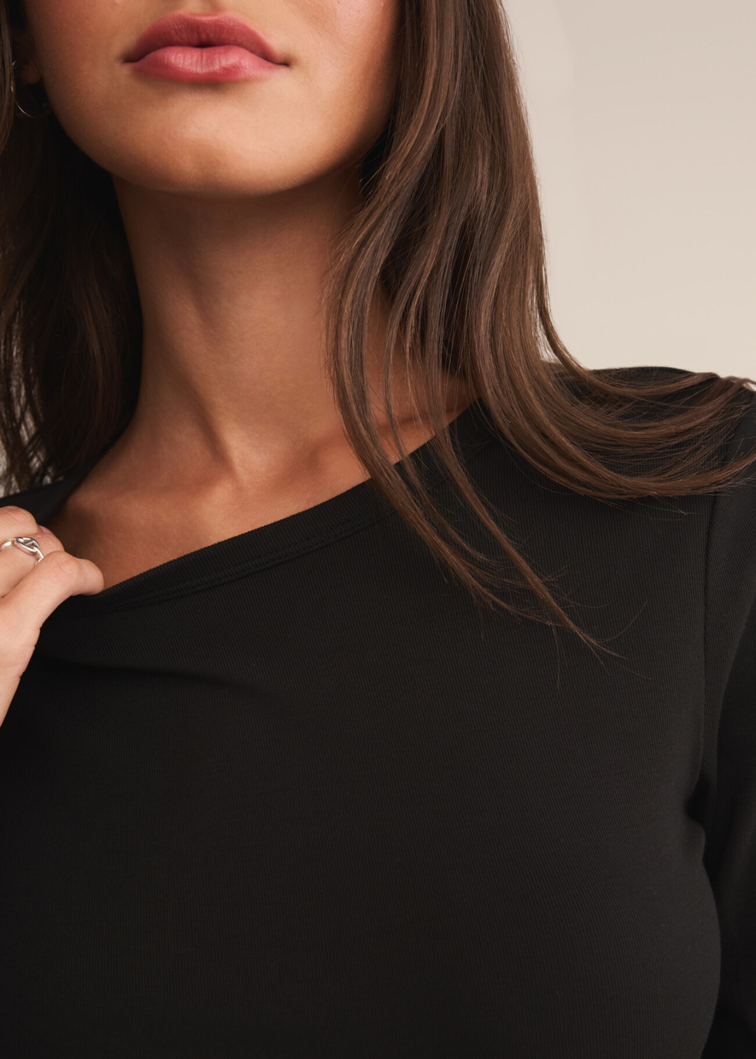 Close up of a woman wearing a black crew neck shirt and holding the neckline