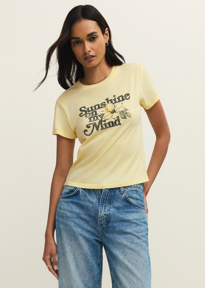 Woman wearing a yellow t-shirt with a "Sunshine on my Mind" graphic and jeans against a grey background