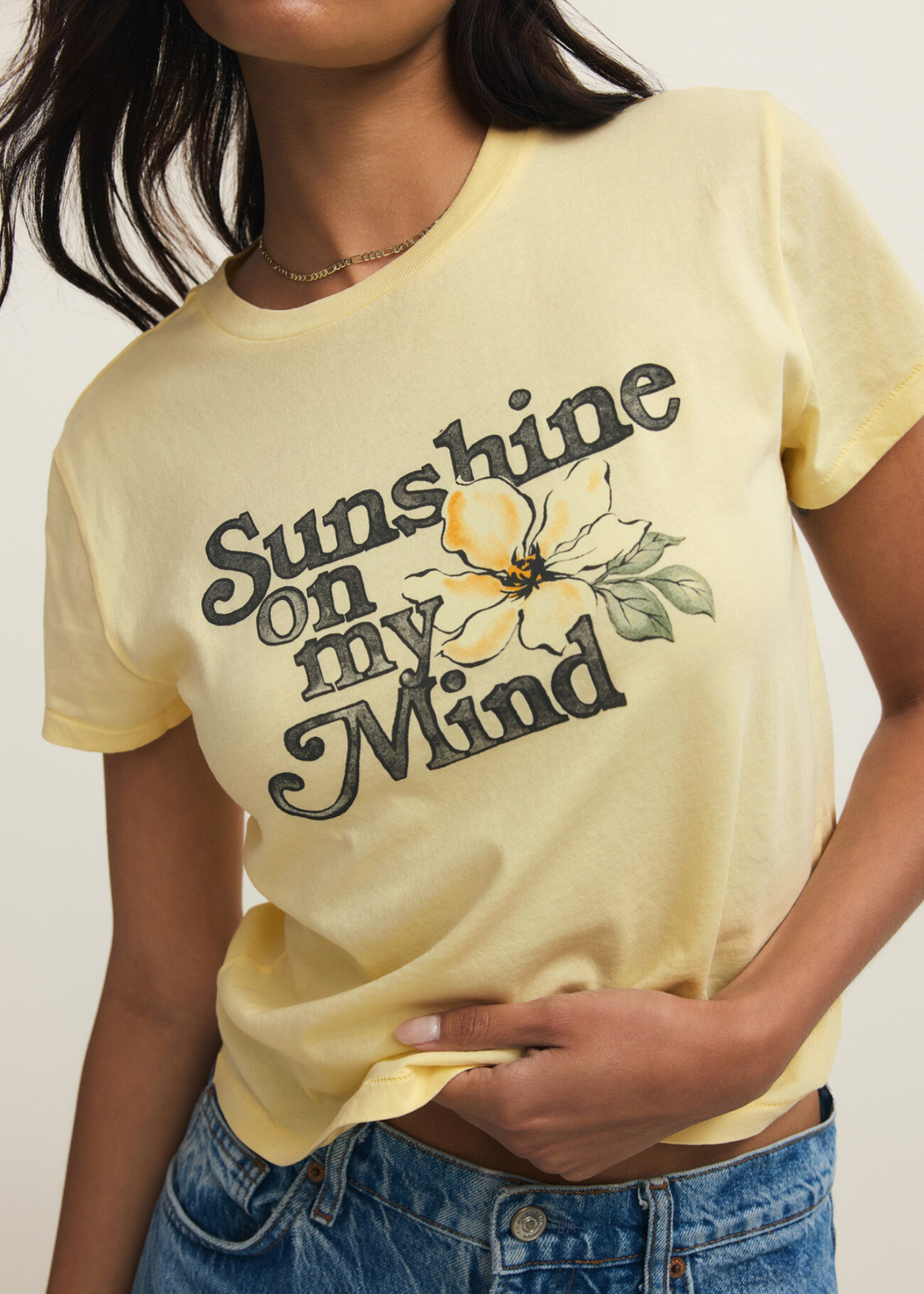 Woman wearing a yellow t-shirt with a "Sunshine on my Mind" graphic and jeans against a grey background