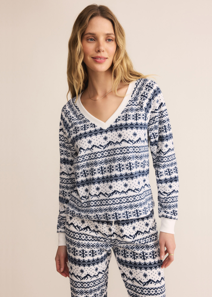 Woman wearing a blue and white fairisle patterned v-neck pajama top with matching pants in front of a tan background