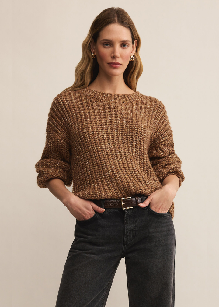 Woman wearing a brown sweater with gold flecks with black jeans standing in front of a white background