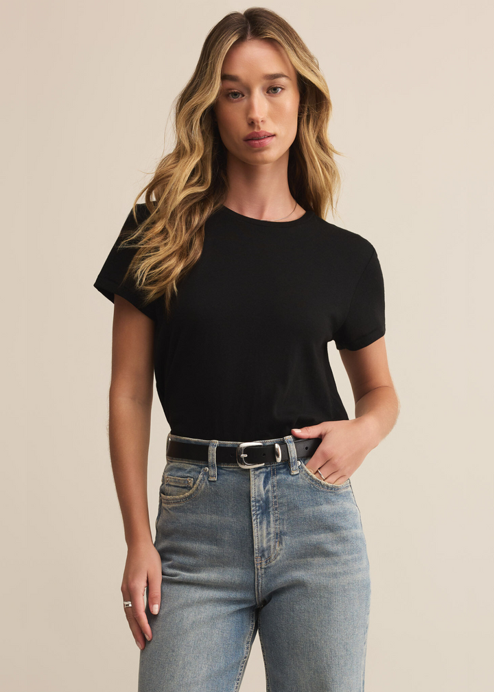 Woman wearing a black short sleeve tee shirt with jeans stranding in front of a tan background