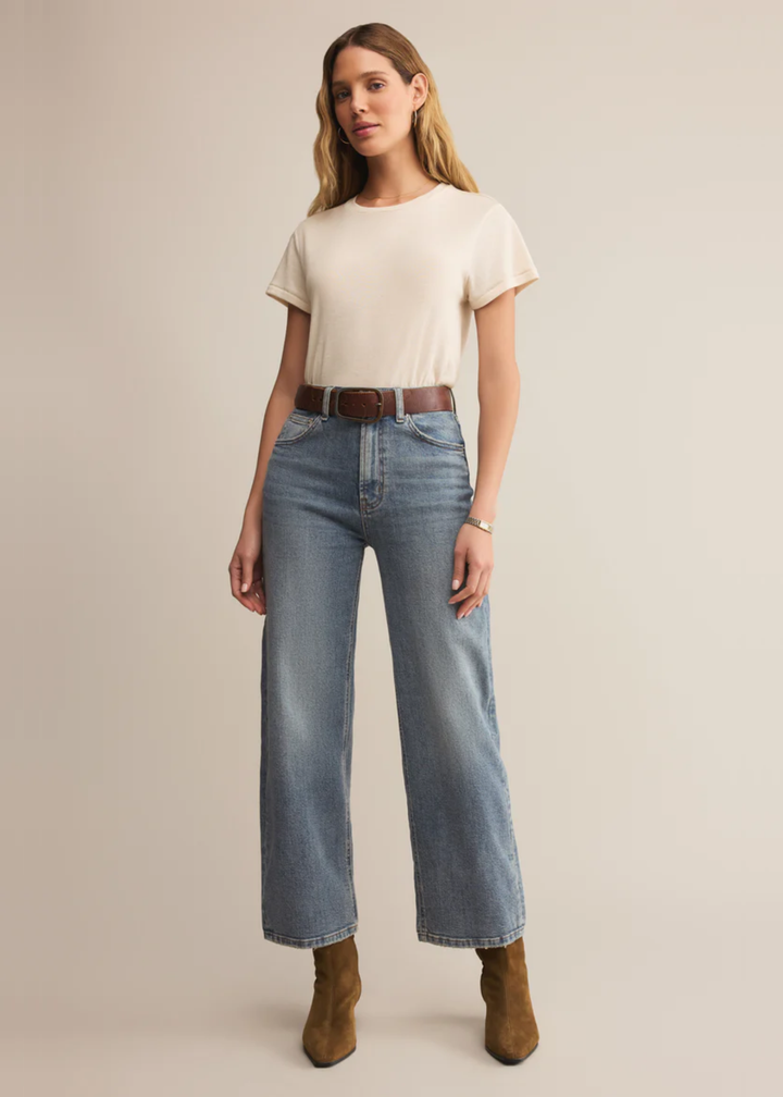 Woman wearing a white short sleeve shirt with jeans and brown boots standing in front of a white background
