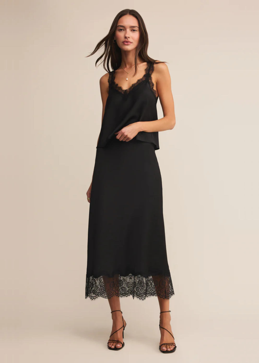 Woman wearing a black satin cami with black lace trim with a matching skirt