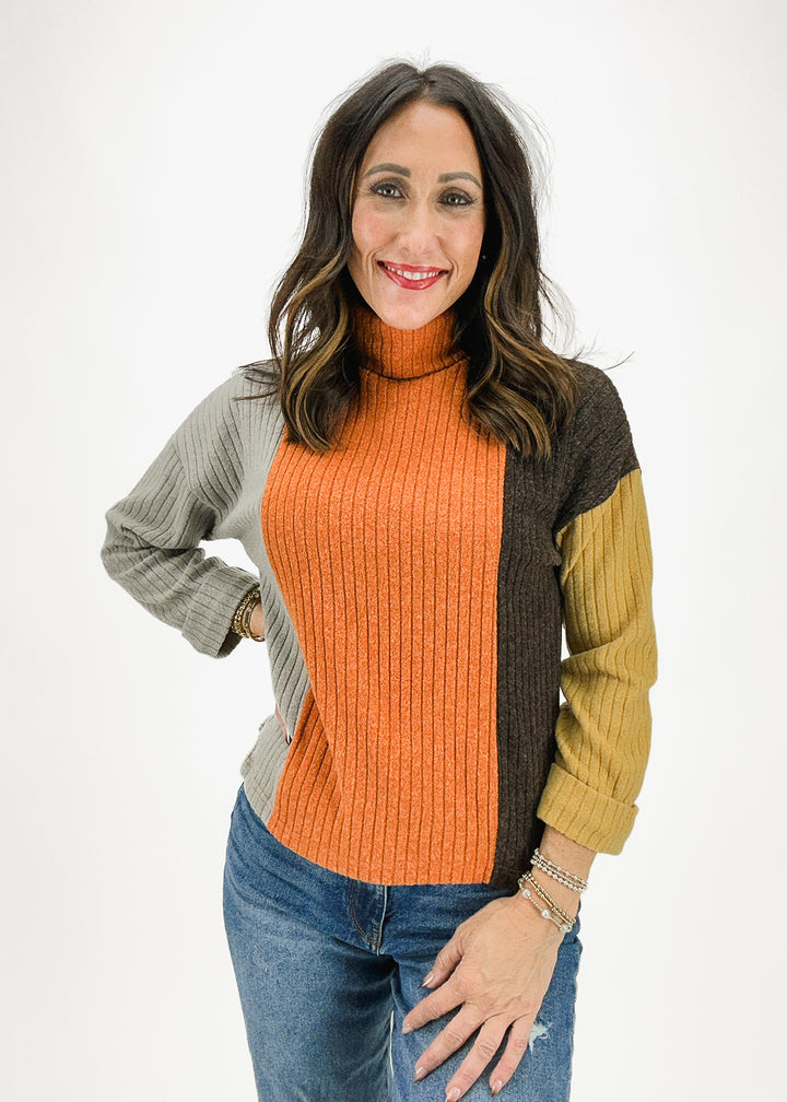 A stylish color-block turtleneck sweater featuring vibrant shades of orange, brown, gray, and yellow, perfect for adding a bold touch to your fall wardrobe.