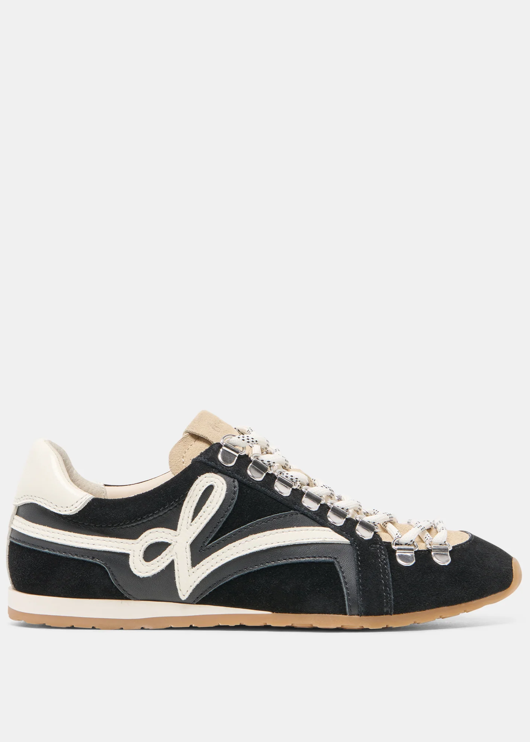 A black suede low-top sneaker with cream-colored panels, a large white script logo on the side, and decorative silver-tone metal eyelets on the laces, shown against a light gray background.