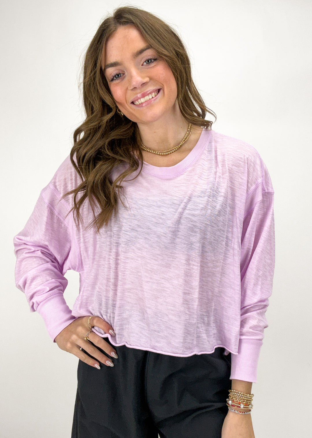 Woman wearing a light purple long-sleeve top and black pants on a white background