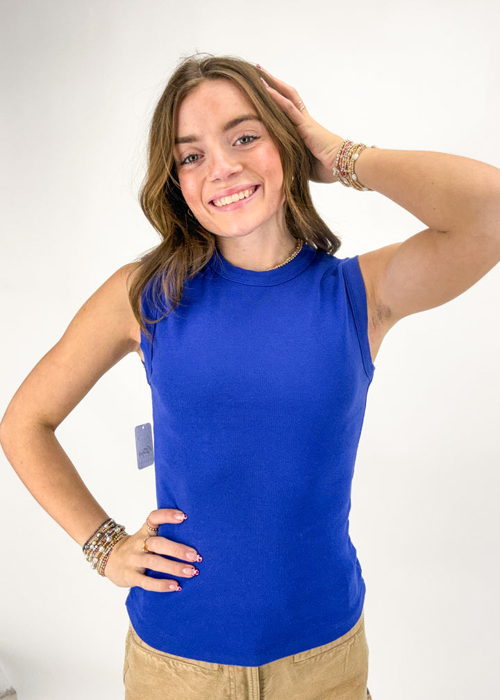 Woman wearing a blue sleeveless top with a visible brand tag on a white background