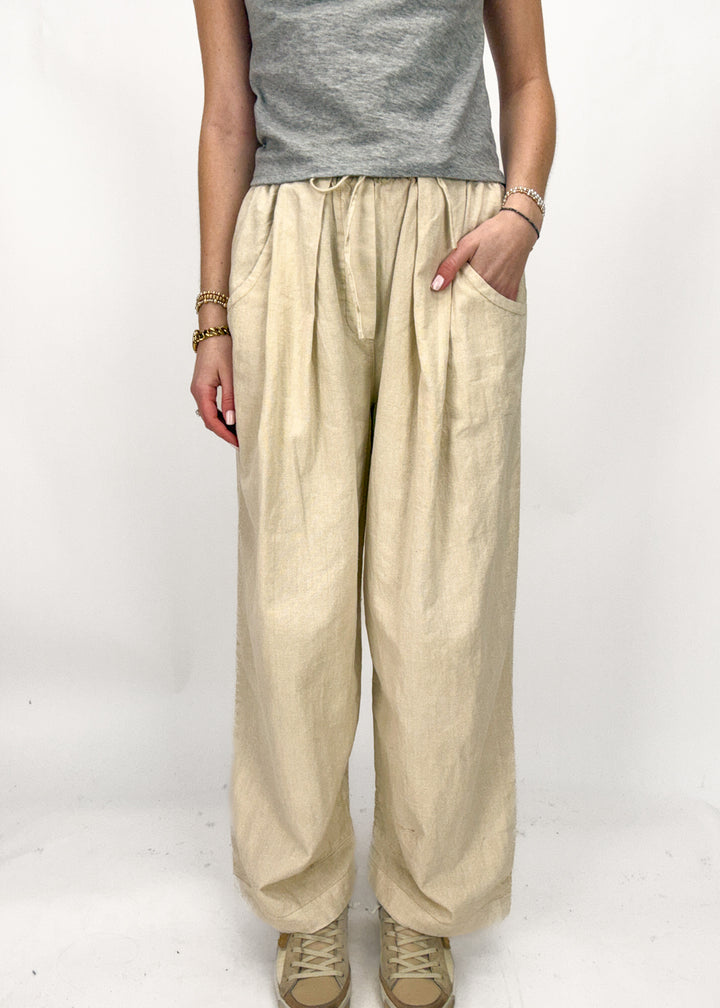 Person wearing beige wide-leg pants and a gray top on a white background
