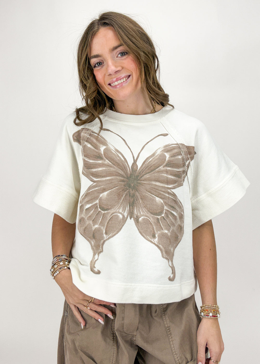 Woman wearing a white t-shirt with a brown butterfly design on a plain background