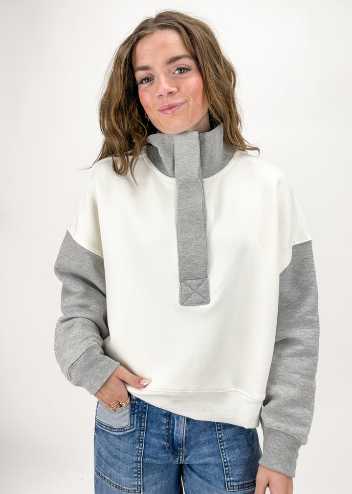 Person wearing a white and gray sweater with blue jeans on a white background