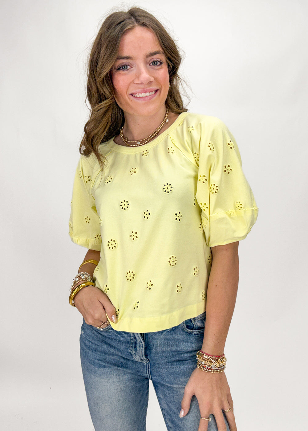 Woman wearing a yellow blouse with floral patterns and blue jeans on a white background