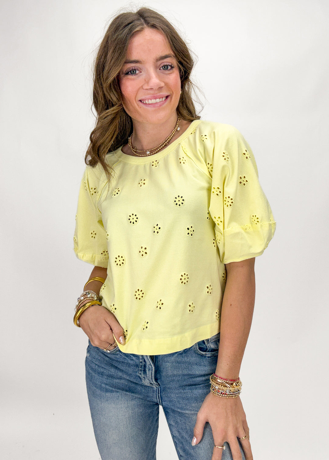 Woman wearing a yellow blouse with floral patterns and blue jeans on a white background