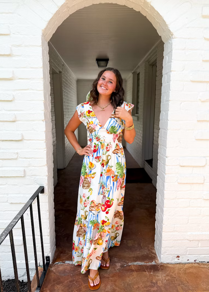 Woman in a floral dress standing in a doorway with a white brick wall background