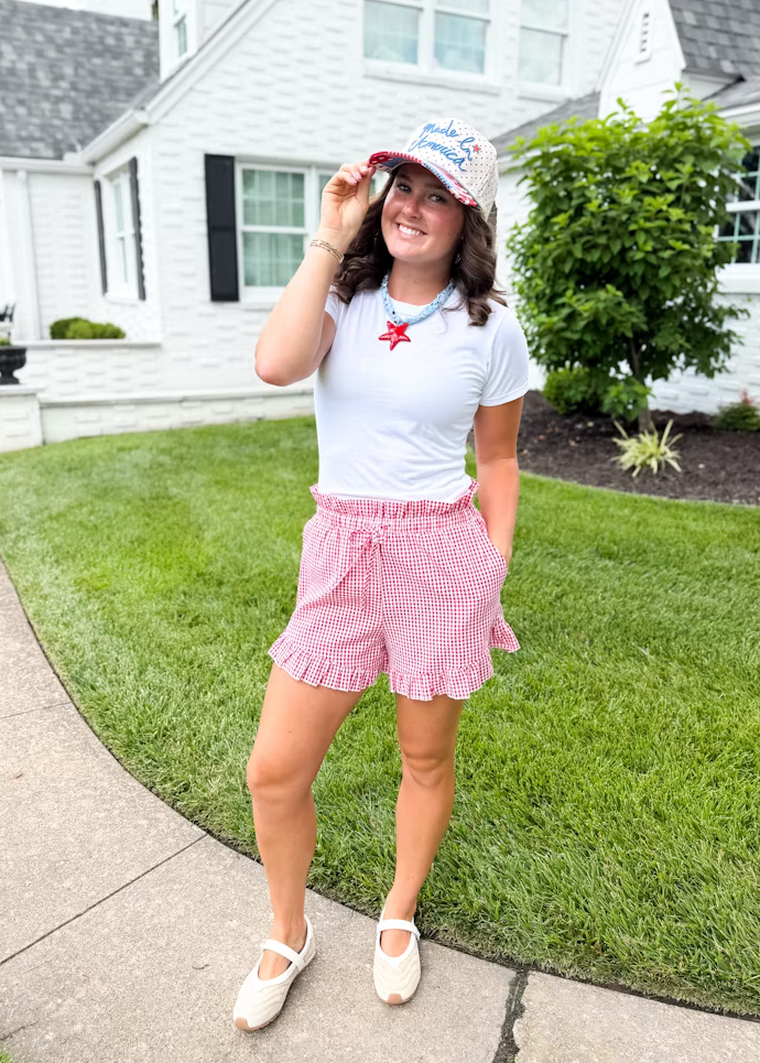 Woman in a white t-shirt and red shorts standing on a grassy lawn in front of a house.