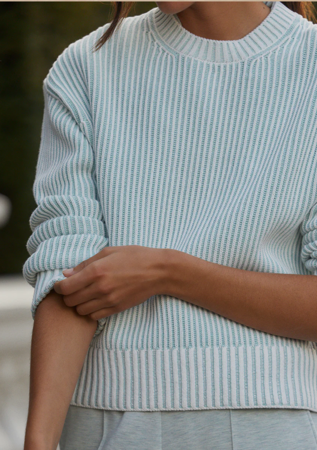 A close-up of a person wearing a light blue and white vertically striped ribbed knit sweater, with the sleeves rolled up.