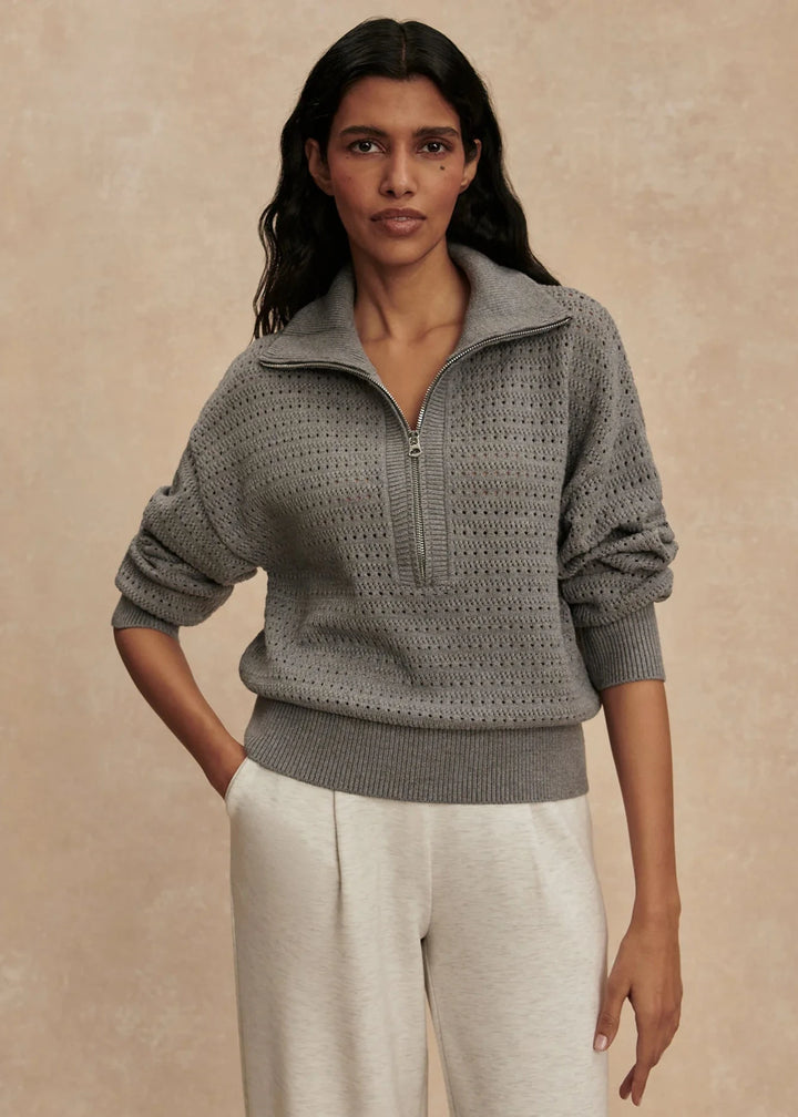 Woman wearing a gray knit sweater with a zipper on a beige background