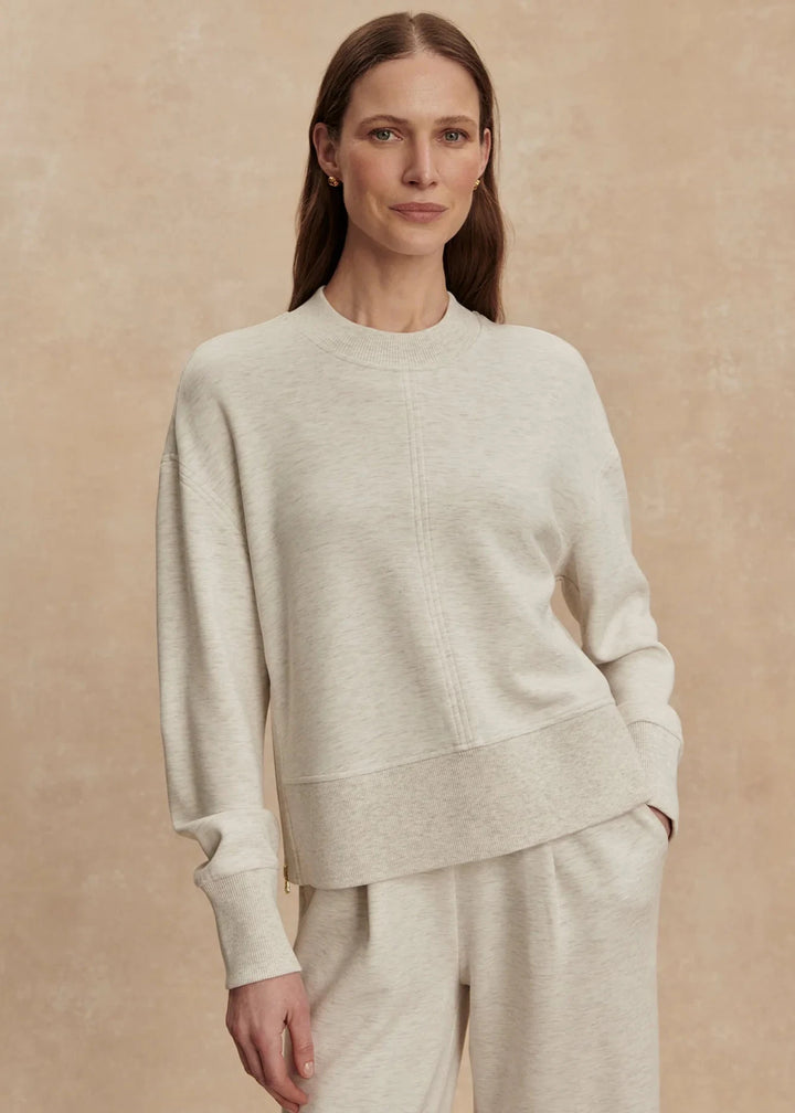 Woman wearing a light gray sweater and pants against a beige background