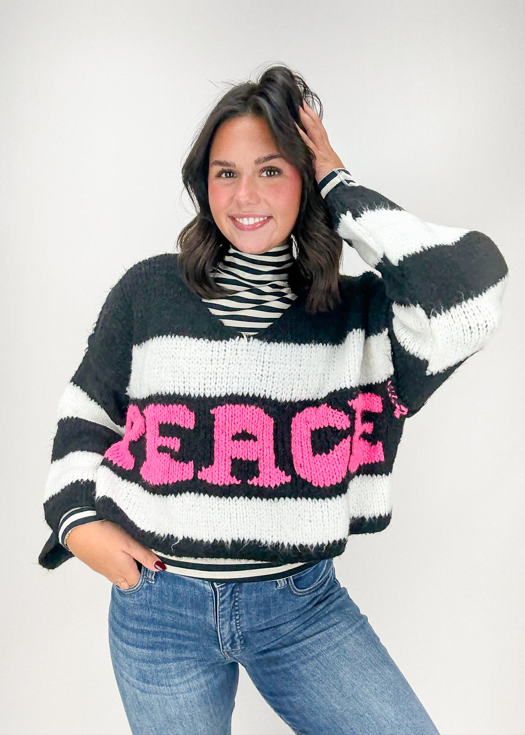Person wearing a black, white, and pink striped sweater with 'PEACE' printed on it.