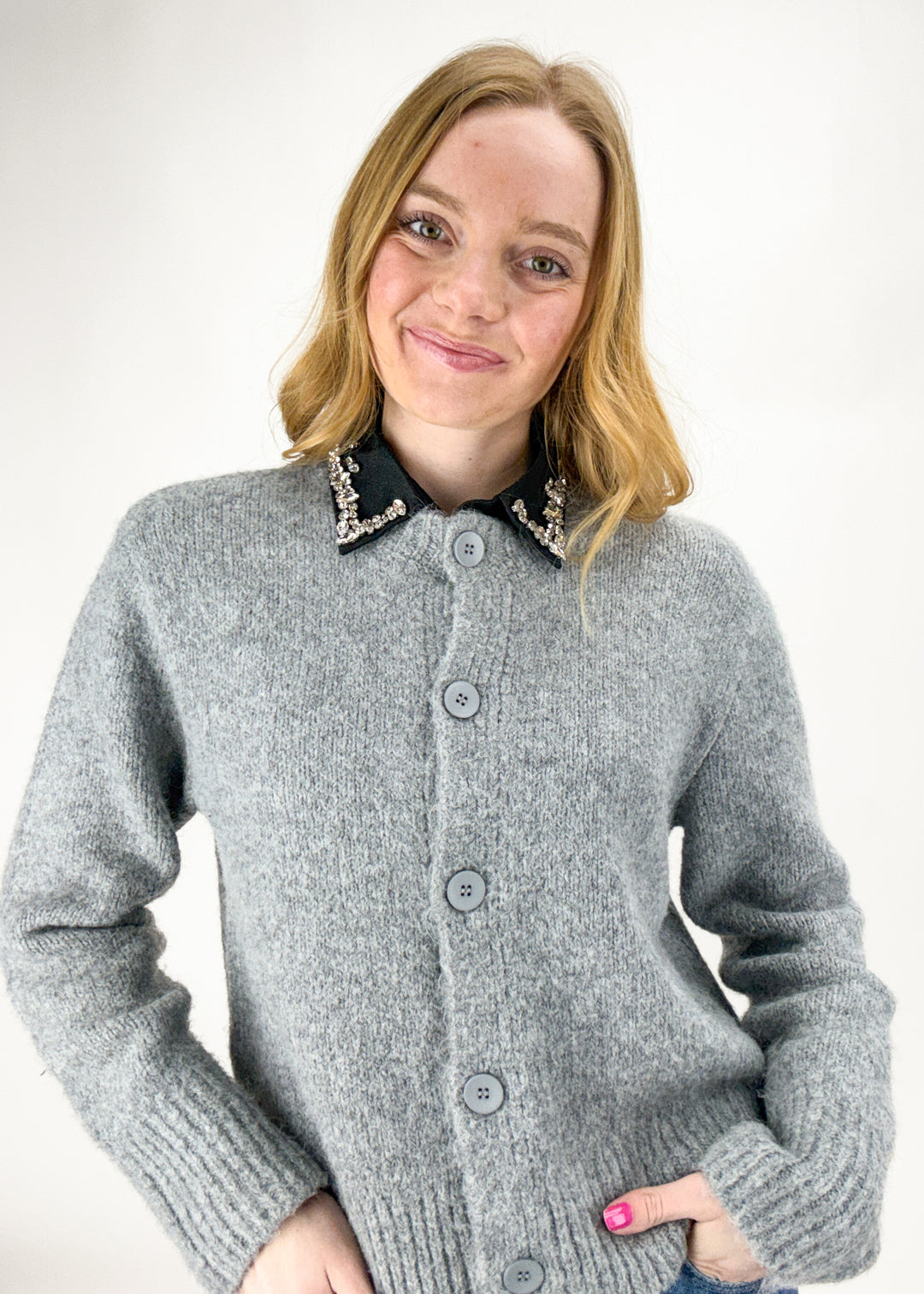 Woman wearing a gray cardigan with a black collar against a white background