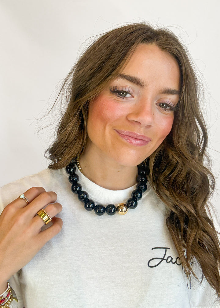 Woman wearing a black beaded necklace with a white top, against a plain background