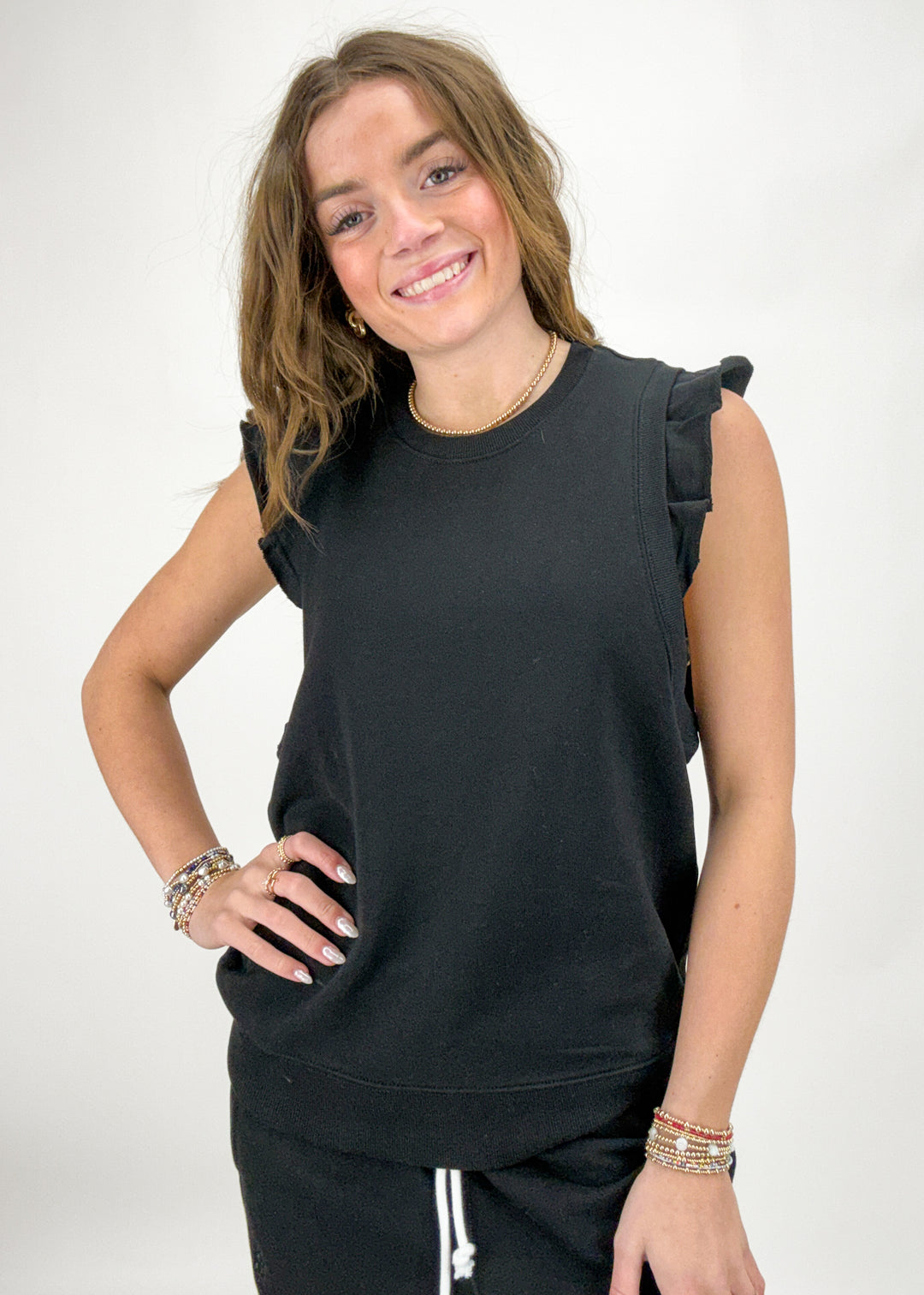 Woman wearing a black sleeveless top with ruffled shoulders on a white background