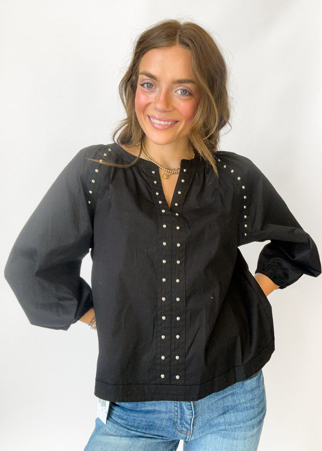 A woman wearing a black long-sleeve blouse with silver stud embellishments on the front and shoulders