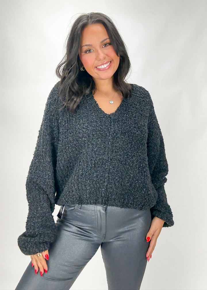 Woman wearing a dark gray sweater and gray pants against a white background