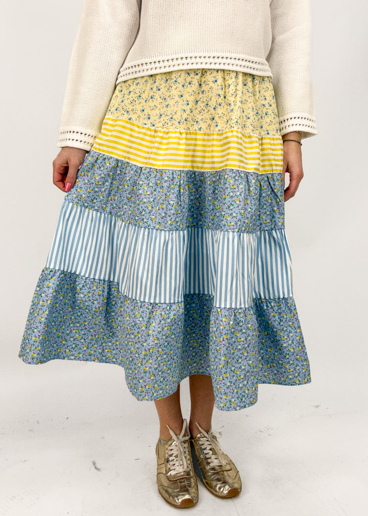 Person wearing a layered skirt with blue, white, and yellow patterns on a plain background