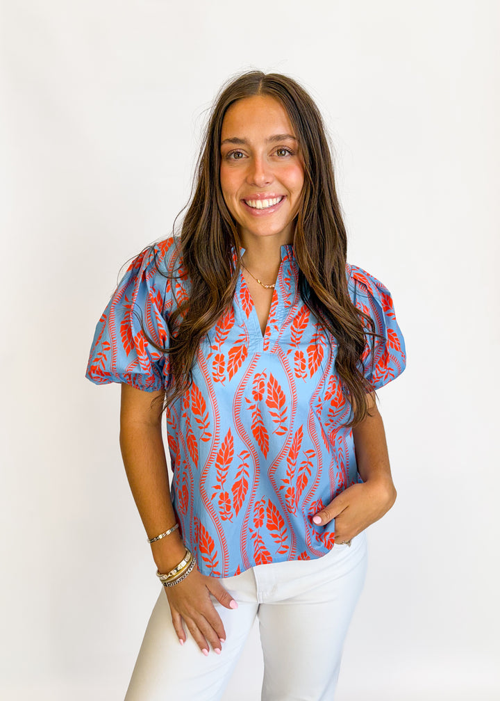 Woman wearing a blue and red patterned blouse with white pants against a white background