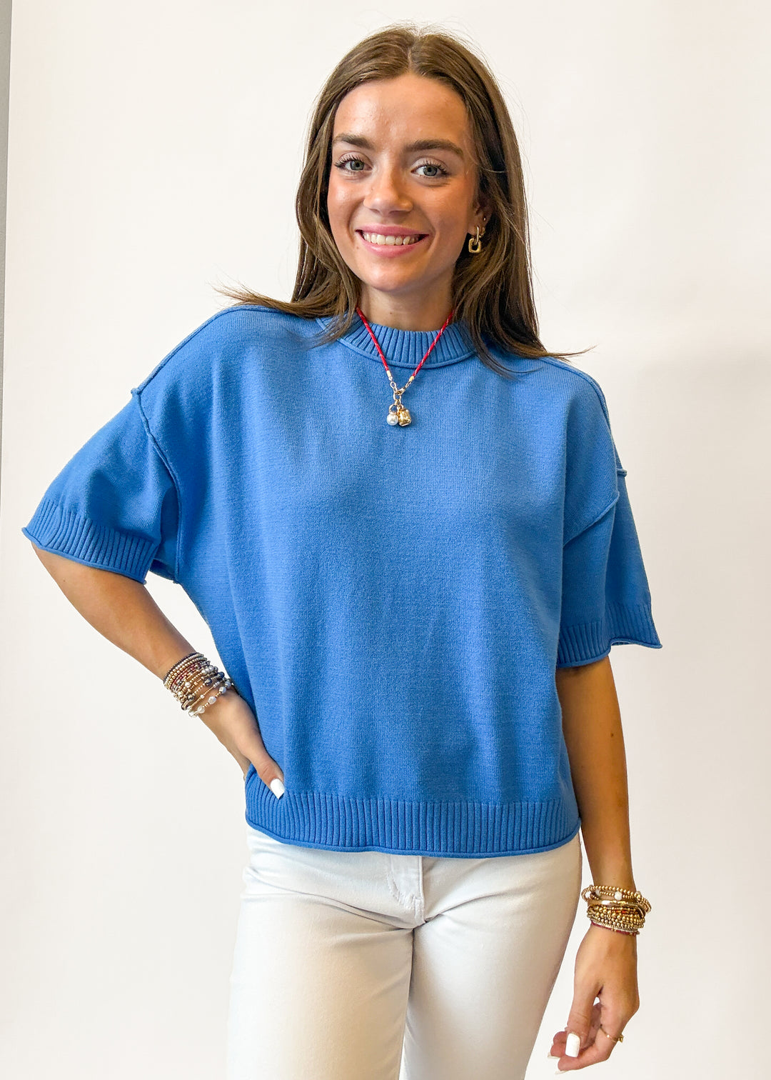 Woman wearing a blue sweater and white pants against a plain background