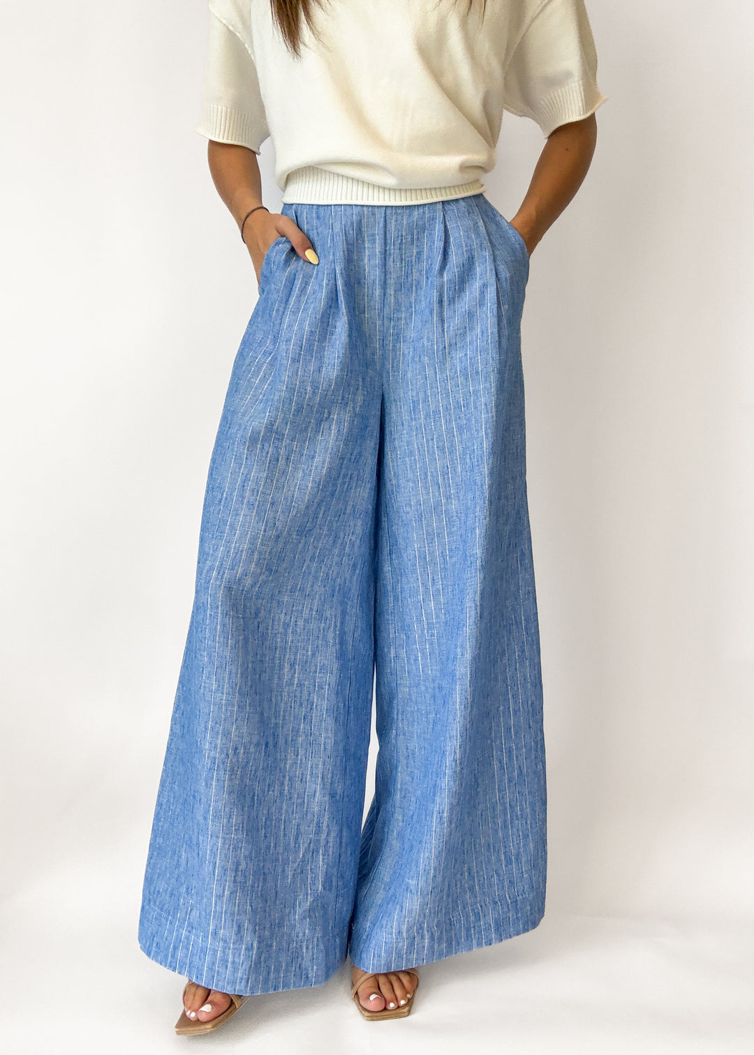 Person wearing blue wide-leg pants and a white top on a white background
