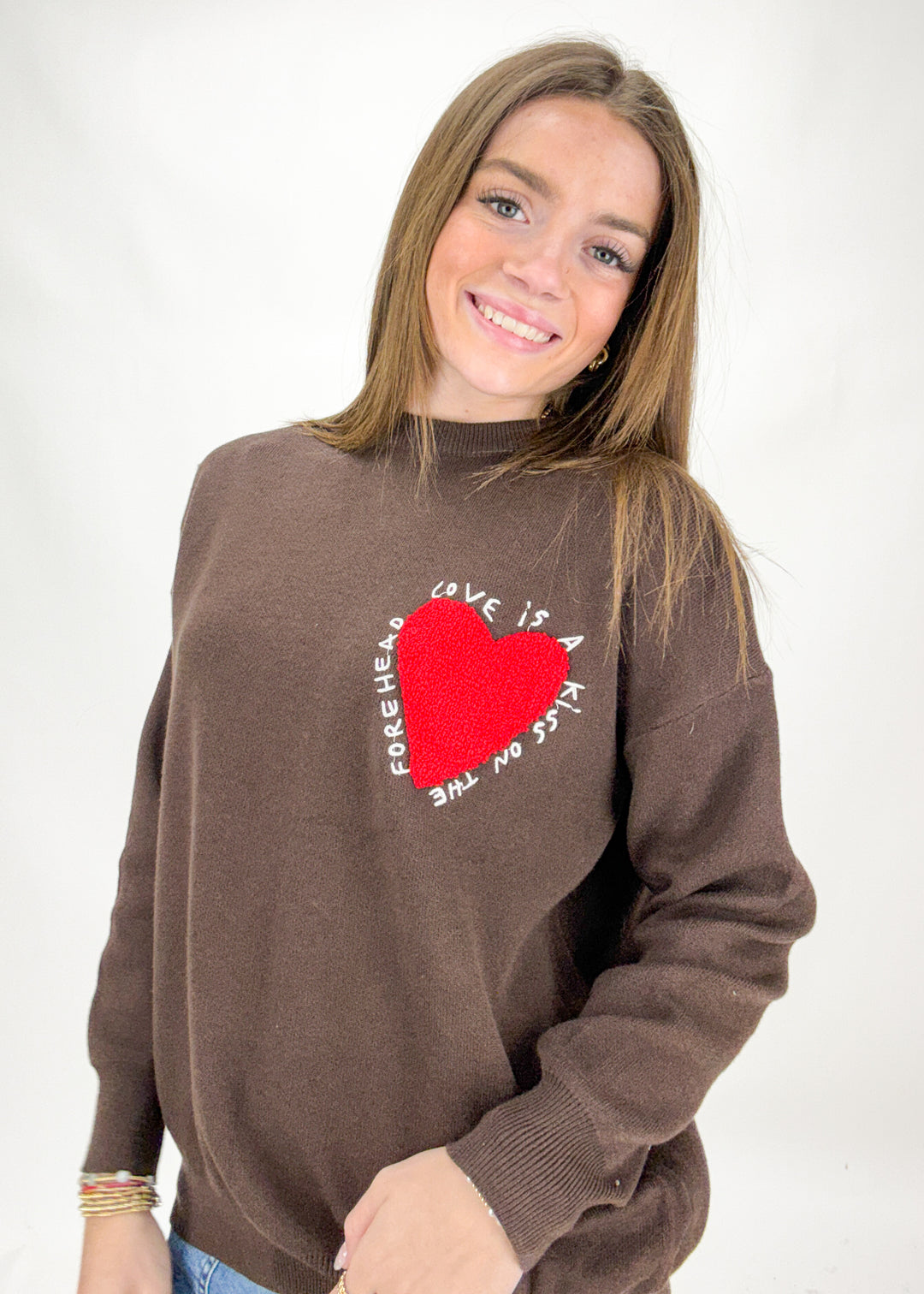 Woman wearing a brown sweater with a red heart design on a white background