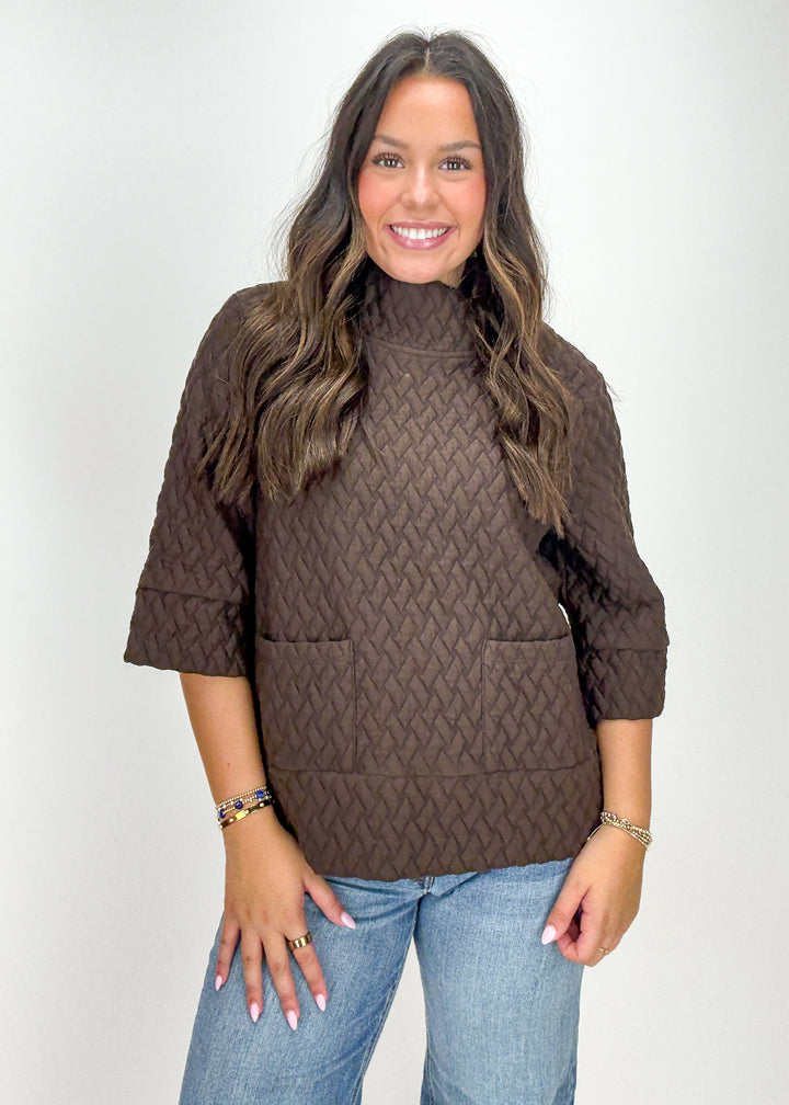 Woman wearing a brown cable knit sweater and blue jeans 