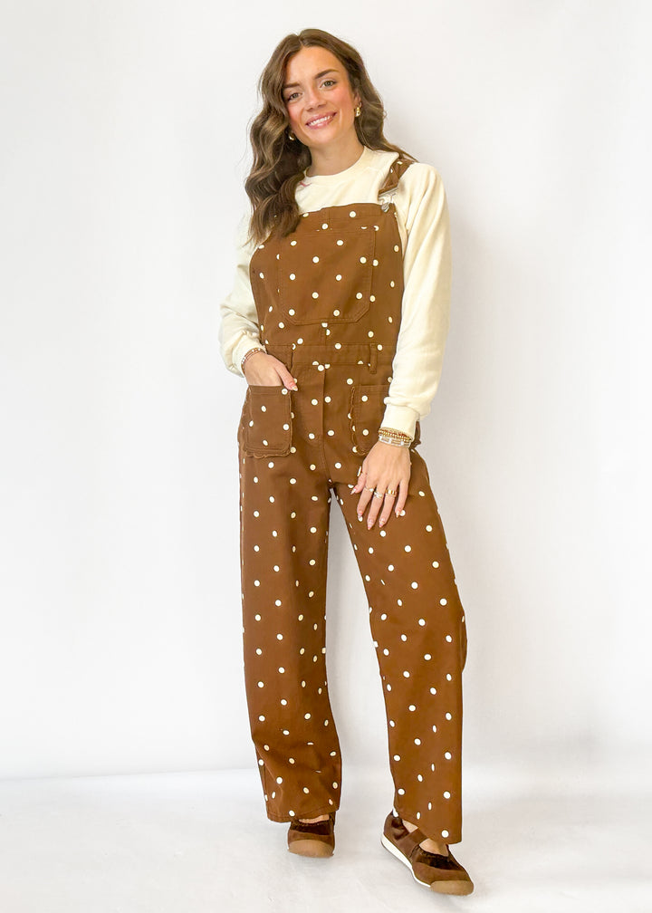 A woman modeling a pair of brown overalls with white polka dots