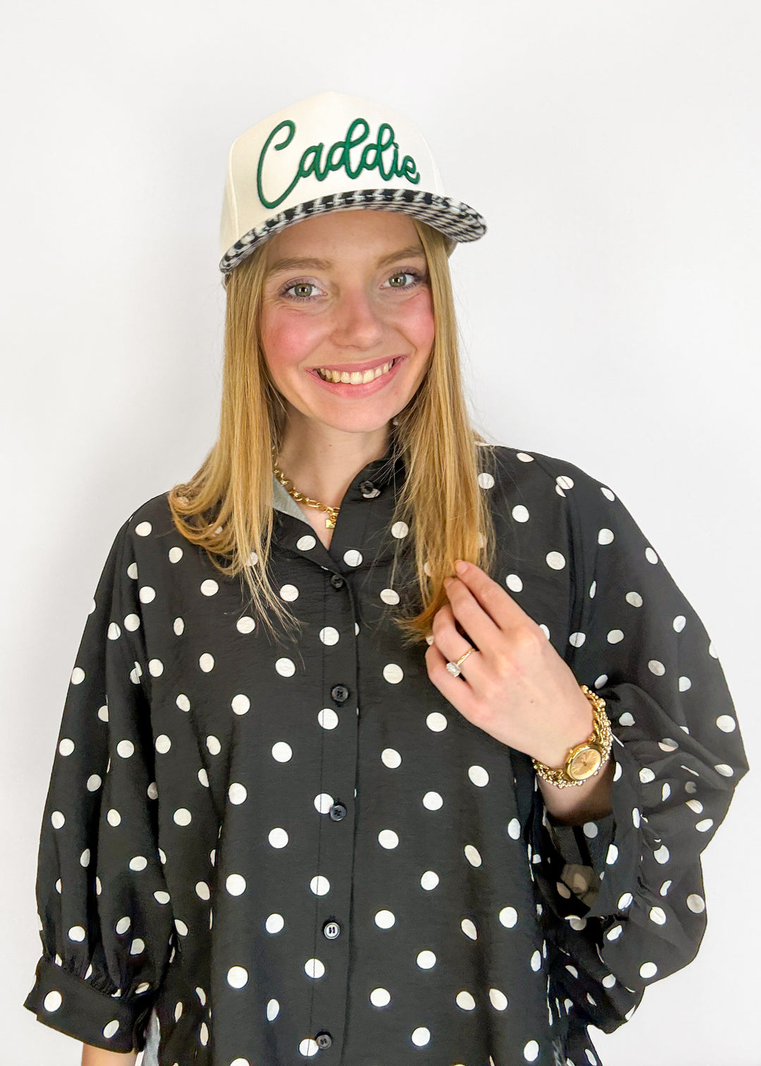 Person wearing a black polka dot shirt and a cap with 'Caddie' text on a white background