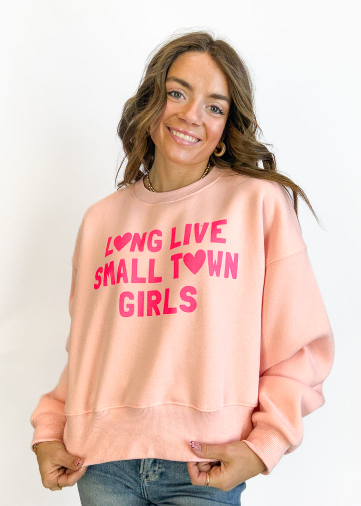 Woman wearing a pink sweatshirt with text, standing against a plain background