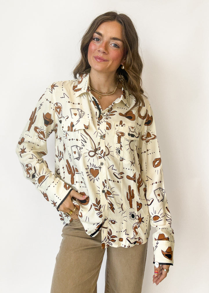 A woman modeling a cream-colored long-sleeve button-up shirt with a brown and black western-themed print