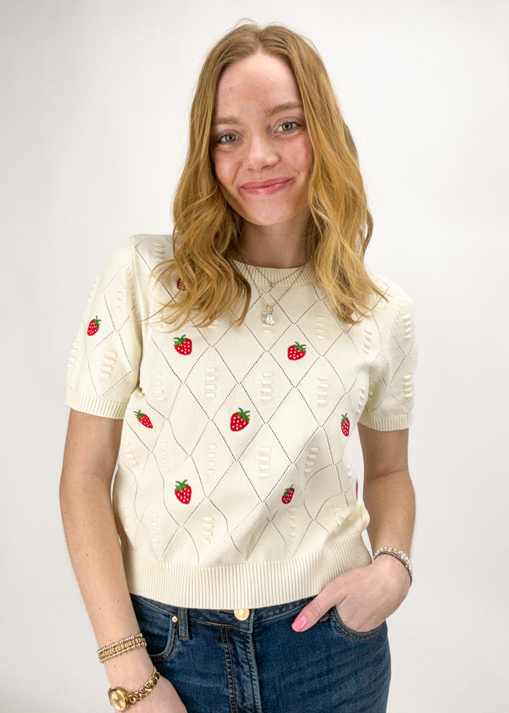 Woman wearing a cream sweater with strawberry patterns on a white background
