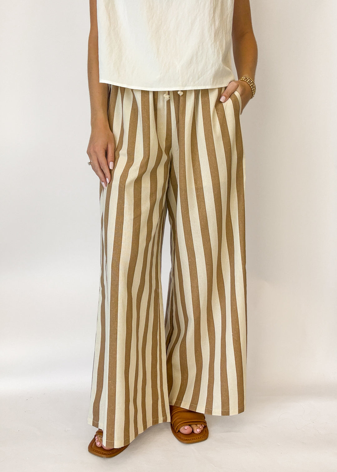 Person wearing a white top and brown and beige striped pants on a plain background